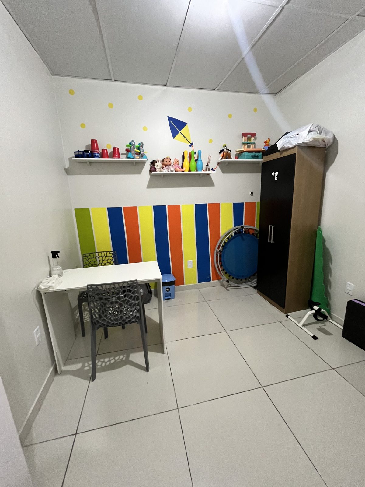 Sala infantil com mesinha, trampolim e brinquedos nas prateleiras