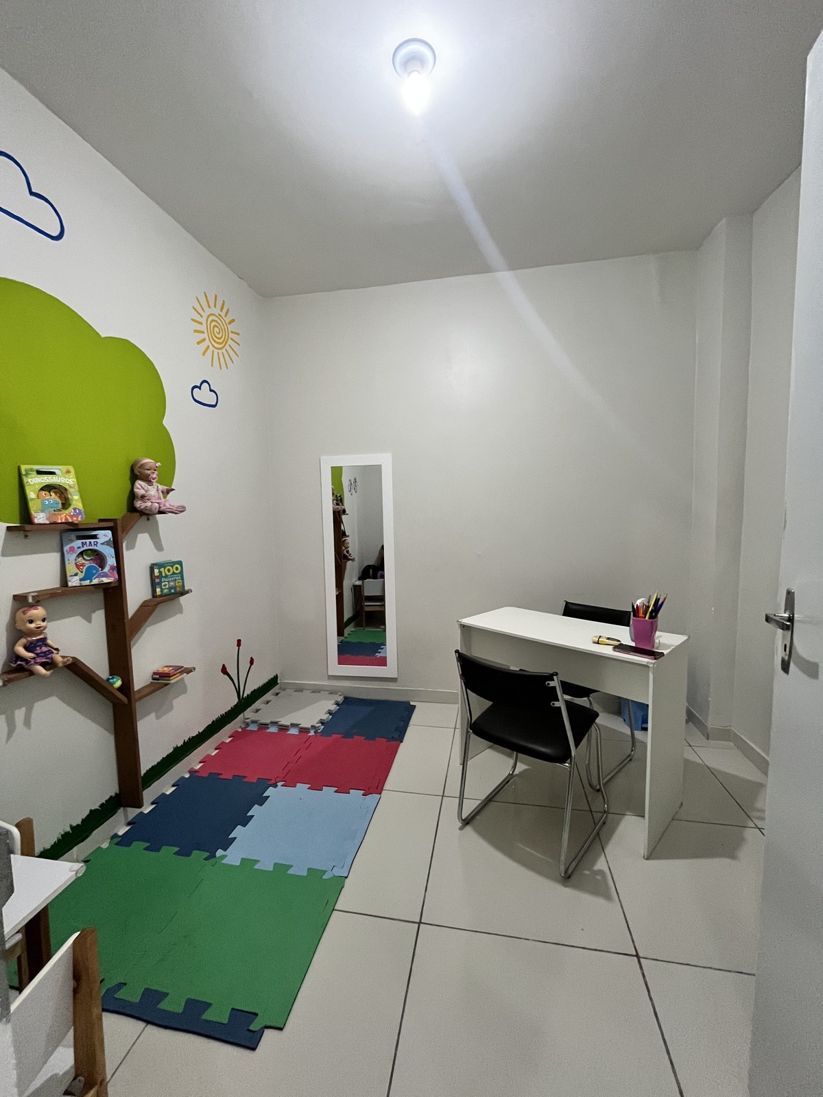 Sala infantil com tatame colorido, estante de brinquedos e mesa de atendimento