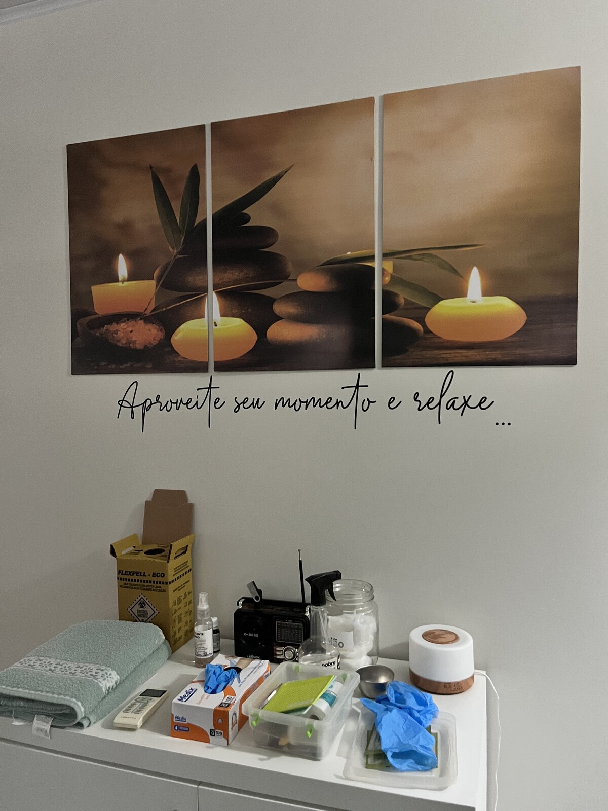 Quadro decorativo de velas sobre armário com toalhas e materiais de atendimento